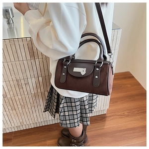 Détail d'un sac seau cylindrique marron foncé avec texture daim et pendentif cœur en métal