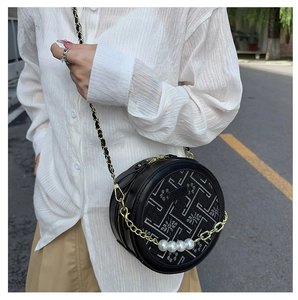 Detail of round black crossbody bag with floral embroidery and pearl chain accent