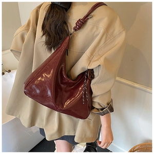 Detailed close-up of glossy burgundy tote bag with stylish knot strap and pleated texture