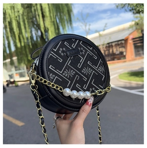 Close-up of black round crossbody bag with floral embroidery, pearls and chain detail