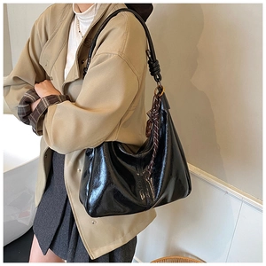 Detail of a shiny black retro hobo bag with knotted wide strap and a striped silk scarf decor