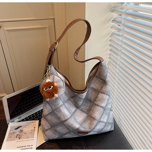 Detail of grey quilted shoulder bag featuring brown leather strap and furry monster charm