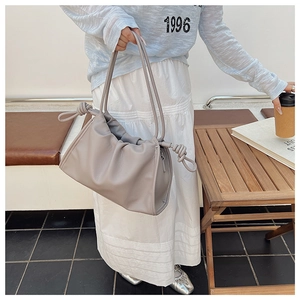 Detailansicht der grauen Plissee-Tasche mit geknoteten Schultergurten in einem Café-Ambiente