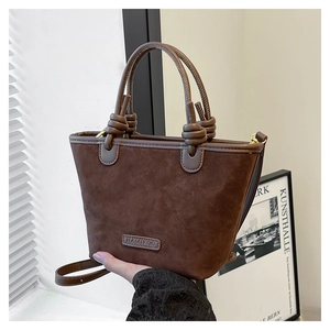 Dettaglio di una borsa a secchiello in pelle scamosciata marrone con logo a rilievo