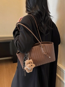 Sac cabas marron tissé avec breloque chien en peluche et anse nouée porté sur un manteau
