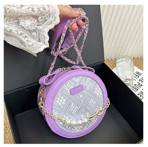 Detail of round purple crossbody bag with pearl accents and gold chain on gift box