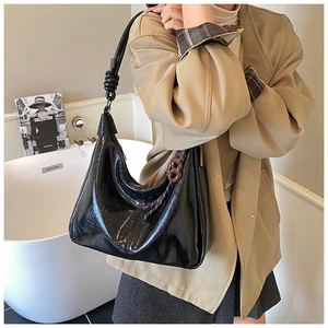 Detail of a black glossy hobo bag with knotted strap and chic brown woven pendant charm