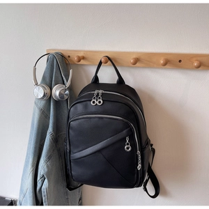 Detail of black pebbled leather backpack with silver ring zippers and denim jacket backdrop