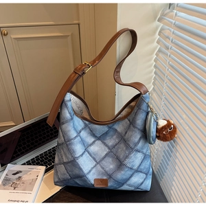Detail of quilted denim underarm bag with brown leather strap and plush charm