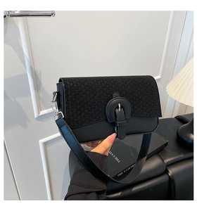 Detail of black quilted shoulder bag featuring woven texture, leather strap and silver hooks
