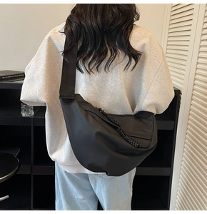 Minimalistische schwarze Halbmond-Umhängetasche an einem Modell mit breitem Gurt