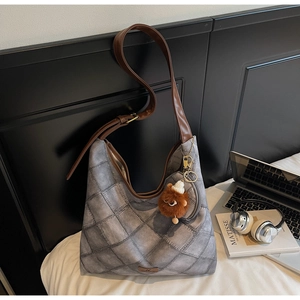 Detail of dark grey quilted tote bag with brown leather strap and plush monster charm