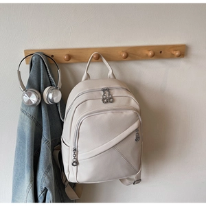 Detail of beige litchi leather backpack featuring multi-zipper compartments and textile straps