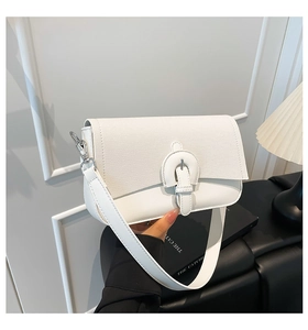 Detail shot of white shoulder bag featuring textured panels and large decorative buckle strap
