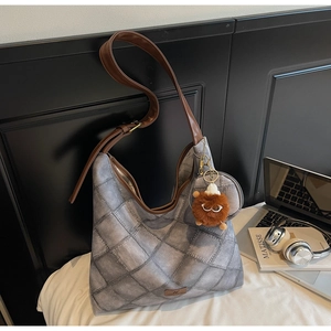 Close-up of gray quilted bucket bag featuring a brown leather strap and plush monster charm