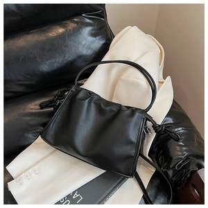 Detail der schwarzen Cloud-Tasche mit Knotendetails vor weißem Blazer-Hintergrund