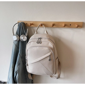 Creamy beige backpack in lychee texture hanging on a wooden hook with lifestyle decor
