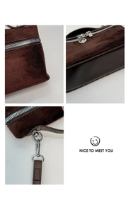 Detail view of dark brown suede handbag with silver metal zippers and strap hooks