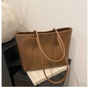 Close-up of caramel brown matte leather tote bag with reinforced stitching on a wood base