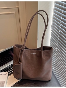 Vintage brown leather tote bag with long strap and small pouch next to a laptop