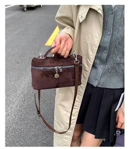 Detail of dark brown suede crossbody bag with silver zipper and brand metal pendant
