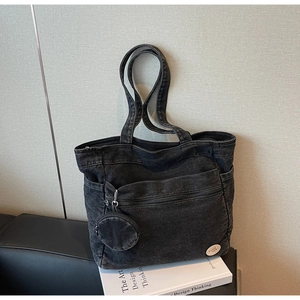 Macro shot of black denim tote bag with circular embroidery detail and mini pouch accessory