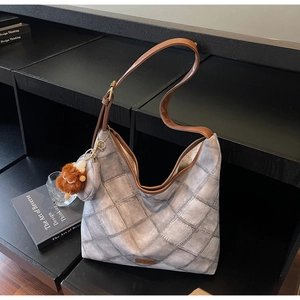 Close-up of quilted grey hobo bag featuring brown leather strap and plush bear charm