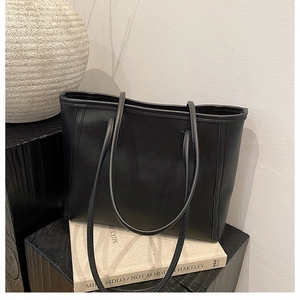 Detail of a minimalist black matte leather tote bag styled on a modern pedestal with books