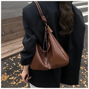 Detail of a brown leather crescent tote bag with knot strap in an autumn street setting