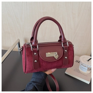 Détail d'un sac seau bordeaux avec pendentif cœur, rivets et textures de cuir lisses
