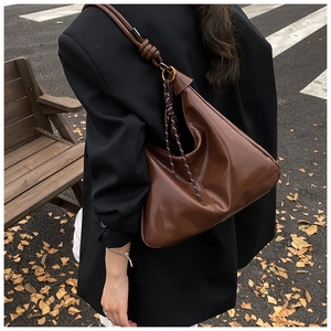 Close-up of brown glossy leather shoulder bag with knot detail and woven rope accent