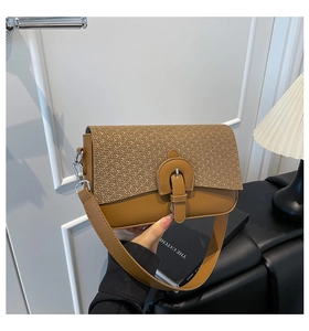 Detail of caramel crossbody bag featuring woven straw flap and vintage buckle strap