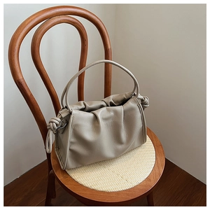 Detail der beigen gerafften Cloud-Tasche mit Knotendetails auf einem Holzstuhl