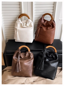 Detalle de cuatro bolsos bombonera de colores con asas de madera y borlas en un banco