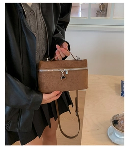 Brown suede-texture handbag with double zippers and metallic circular charm on a wooden table