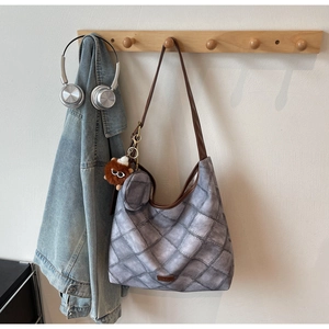 Detailed view of grey quilted tote bag with brown leather strap and plush bear charm