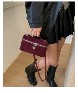 Detail of burgundy suede handbag showing top handle and silver zipper with round pendant