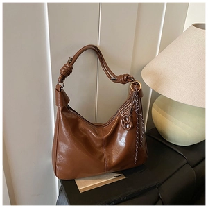 Close-up of caramel brown oil-wax leather hobo bag with knotted strap and tassel detail