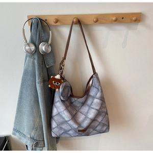 Detail of grey checkered tote bag with brown leather straps and plush bear charm