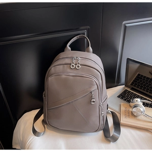 Detail of grey pebbled leather backpack with silver zippers and metal chain charm