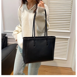 Chic black tote bag with long handles shown in a minimalist interior setting