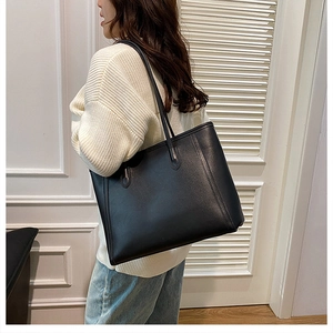Classic large black leather tote bag shown on shoulder in a lifestyle indoor setting