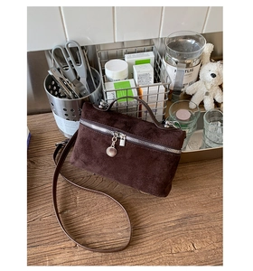 Detail of dark brown suede crossbody bag featuring a silver zipper and round metal pendant