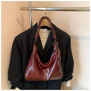 Detail of burgundy glossy leather hobo bag with unique knotted handle hanging on a suit