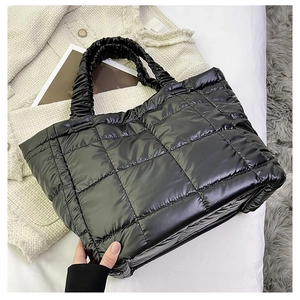 Close-up of black quilted puffer tote bag with ruched handles on white bedding