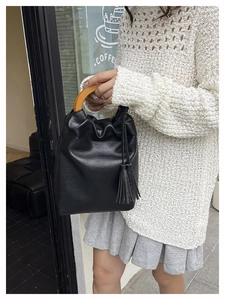 Detalle del bolso tipo cubo negro con asa de madera vintage y borla decorativa lateral