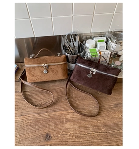 Detailed macro view of matte suede handbags in camel and dark brown with silver zippers
