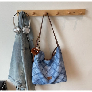 Quilted blue denim tote bag detail featuring brown leather straps and a plush monster charm