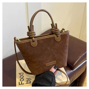 Dettaglio di una borsa a secchiello in camoscio marrone con nodo in pelle e logo