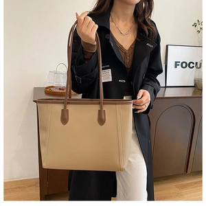 Detail of a large capacity tote bag featuring beige body with brown trim and long shoulder straps